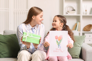 Cute little girl with greeting card for Mother's Day and her mom at home