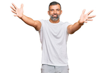 Naklejka premium Middle age handsome man wearing casual white tshirt looking at the camera smiling with open arms for hug. cheerful expression embracing happiness.