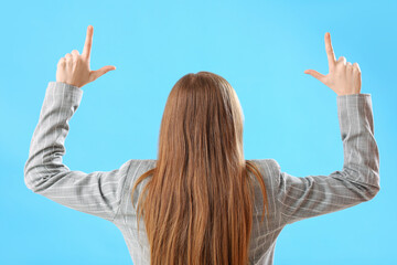 Young businesswoman showing loser gesture on blue background, back view