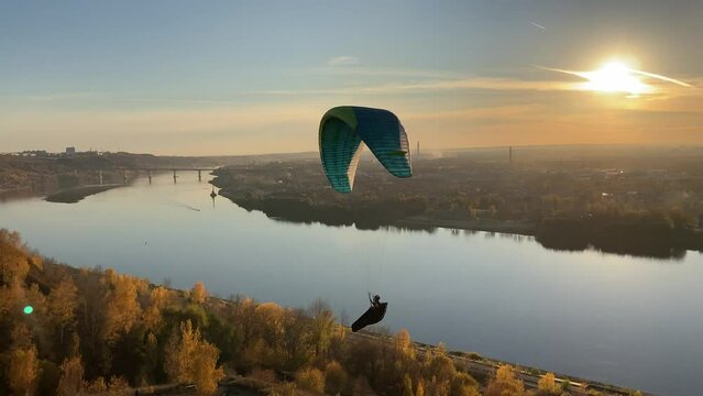Aerial scene from the park "Switzerland" in Nizhny Novgorod with a paraglider soaring above the Oka river towards the Upper City hills covered by autumn forests leaving the backlit Lower City behind
