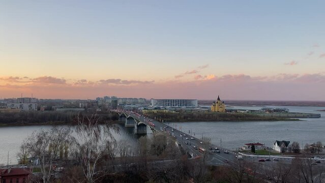 View from Fedorovsky Embankment in Nizhny Novgorod at traffic crossing the Oka river on the Kanavinsky Bridge, the Stadium, the Alexander Nevsky Cathedral and urban houses during an autumn afterglow