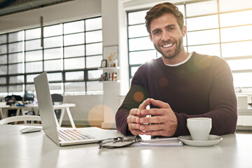 This smile is testament to my success. Portrait of a young businessman working at his desk in a...