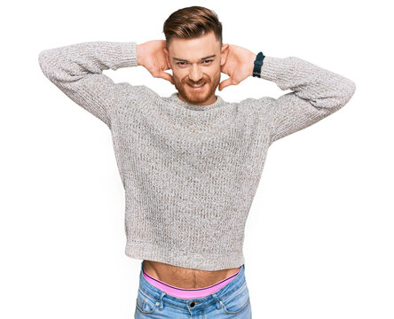 Young redhead man wearing casual winter sweater relaxing and stretching, arms and hands behind head and neck smiling happy