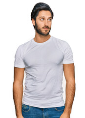 Obraz premium Young hispanic man wearing casual white t shirt smiling looking to the side and staring away thinking.