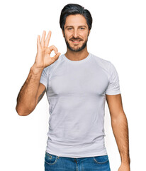 Young hispanic man wearing casual white t shirt smiling positive doing ok sign with hand and fingers. successful expression.