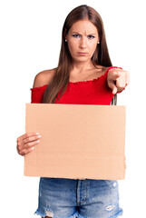 Young beautiful hispanic woman holding banner cardboard pointing with finger to the camera and to you, confident gesture looking serious