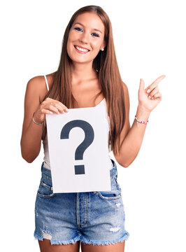 Young beautiful hispanic woman holding question mark smiling happy pointing with hand and finger to the side