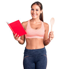 Young beautiful hispanic woman wearing gym clothes reading cooking recipe book holding spoon looking positive and happy standing and smiling with a confident smile showing teeth