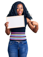 Beautiful african american woman holding blank empty banner smiling happy pointing with hand and finger