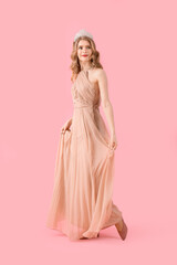 Teenage girl in tiara and prom dress on pink background