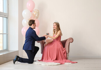 Teenage boy tying corsage around his girlfriend's wrist for prom in room
