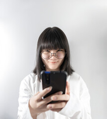 Isolated Pretty Asian glasses woman looks at camera and holds mobile phone in her hand on white background in studio light.