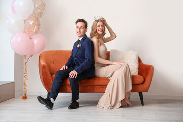 Beautiful couple dressed for prom sitting on sofa in room © Pixel-Shot