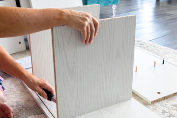 A woman builds and assembles pre-fabricated pieces of desk furniture using a screwdriver inside a...