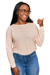 Young black woman wearing casual clothes and glasses smiling with happy face looking and pointing to the side with thumb up.