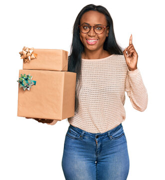 Young black woman holding gifts surprised with an idea or question pointing finger with happy face, number one
