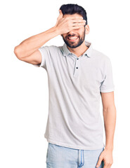 Fototapeta premium Young handsome man with beard wearing casual polo smiling and laughing with hand on face covering eyes for surprise. blind concept.