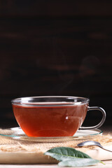 Aromatic hot tea in glass cup and leaves on wooden table against dark background. Space for text