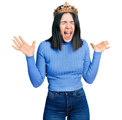Young brunette woman with blue eyes wearing princess crown celebrating mad and crazy for success with arms raised and closed eyes screaming excited. winner concept © Krakenimages.com