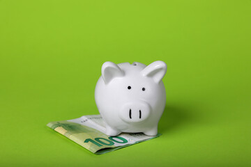 Ceramic piggy bank and euro banknote on light green background. Financial savings