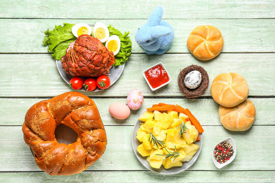 Tasty dishes and painted eggs for Easter dinner on color wooden background