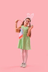 Cute little girl in bunny ears with basket of Easter eggs on pink background