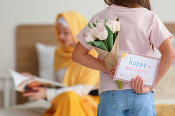Little girl with greeting card for Mother's Day and tulips in bedroom, back view