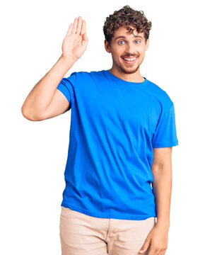 Young handsome man with curly hair wearing casual clothes waiving saying hello happy and smiling, friendly welcome gesture