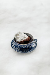 hot chocolate in blue and white Japanese teacup and saucer topped with meringue sitting outside in the snow
