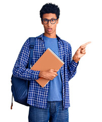 Young african american man wearing student backpack holding book surprised pointing with finger to the side, open mouth amazed expression.