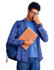 Young african american man wearing student backpack holding book tired rubbing nose and eyes feeling fatigue and headache. stress and frustration concept.