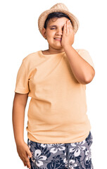 Little boy kid wearing summer hat and hawaiian swimsuit covering one eye with hand, confident smile on face and surprise emotion.