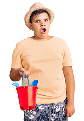 Little boy kid playing with summer shovel and bucket toys scared and amazed with open mouth for surprise, disbelief face