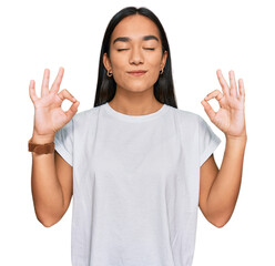 Young asian woman wearing casual white t shirt relax and smiling with eyes closed doing meditation gesture with fingers. yoga concept. - obrazy, fototapety, plakaty