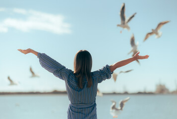 Happy Tourist Admiring Seagulls in Flight Above the Sea. Carefree woman holding her arms up...