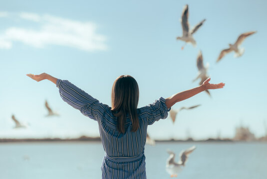 Happy Tourist Admiring Seagulls in Flight Above the Sea. Carefree woman holding her arms up watching birds fly

