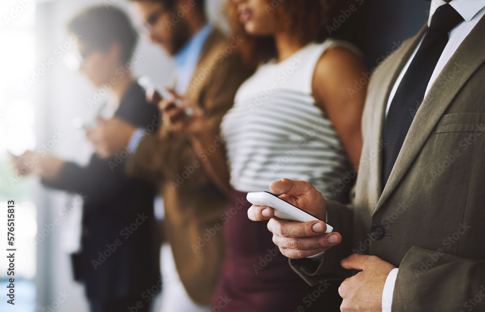 Poster Keep track of industry developments just by logging in. Shot of a businessperson using his cellphone with colleagues blurred in the background.