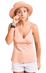 Young blonde woman wearing summer hat mouth and lips shut as zip with fingers. secret and silent,...