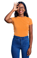 Young indian girl wearing casual clothes and glasses doing ok gesture with hand smiling, eye looking through fingers with happy face.