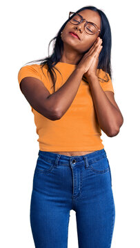 Young indian girl wearing casual clothes and glasses sleeping tired dreaming and posing with hands together while smiling with closed eyes.
