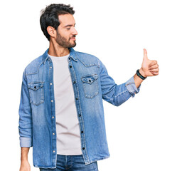 Young hispanic man wearing casual clothes looking proud, smiling doing thumbs up gesture to the side