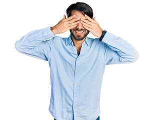 Hispanic man with blue eyes wearing business shirt covering eyes with hands smiling cheerful and funny. blind concept.
