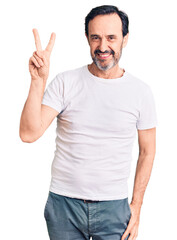 Middle age handsome man wearing casual t-shirt smiling looking to the camera showing fingers doing victory sign. number two.