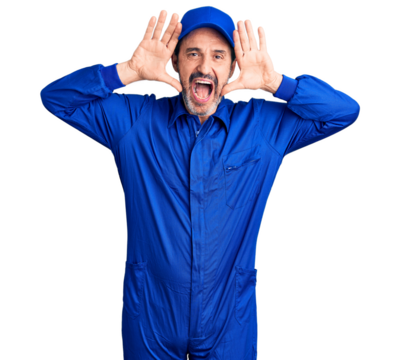 Middle age handsome man wearing mechanic uniform smiling cheerful playing peek a boo with hands showing face. surprised and exited