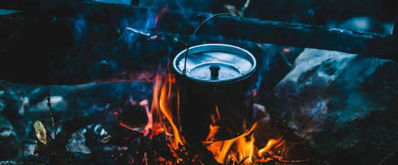 Kettle in soot hanging over fire. Cooking food at fire in wild. Beautiful firewoods burn in bonfire...