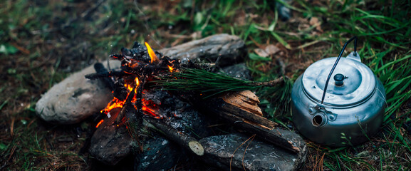 Camping kettle near small camp fire close-up. Cozy camping place in wild. Wonderful evening atmospheric background of campfire. Beautiful flame of small magic bonfire. Romantic warm place with fire.
