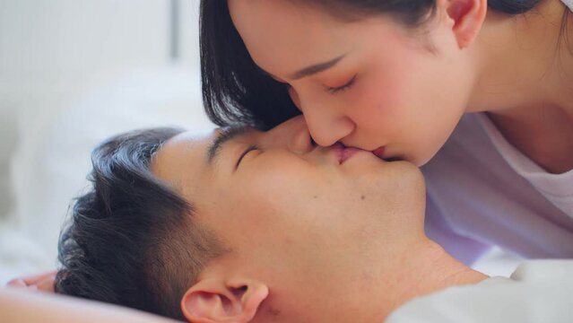 Asian wife kissing her husband while lying down sleep on bed in bedroom