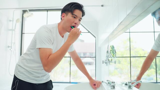Asian young man brushing teeth and look at mirror in bathroom at home.