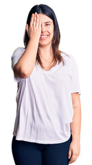 Fototapeta premium Young beautiful brunette woman wearing casual t-shirt covering one eye with hand, confident smile on face and surprise emotion.