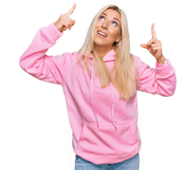 Young blonde woman wearing casual sweatshirt smiling amazed and surprised and pointing up with fingers and raised arms.